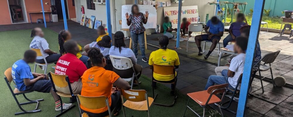 Elorm leading an Autism Awareness Training session with participants seated in a circle.